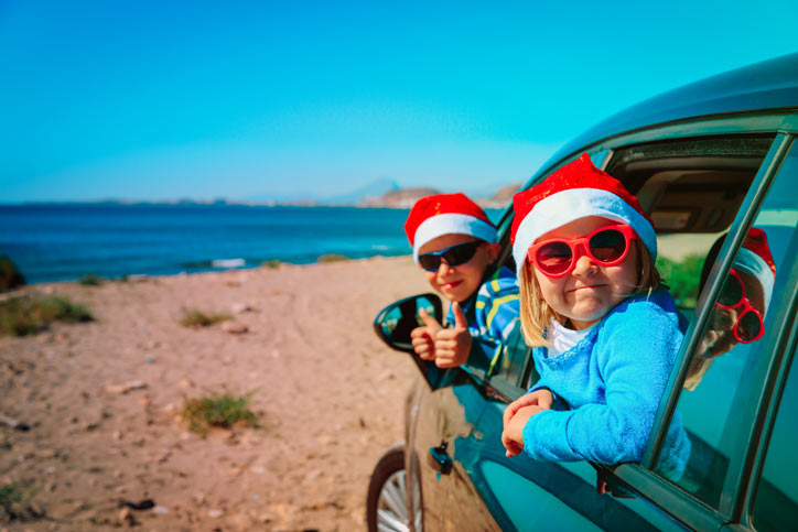 A car on the beach with kids hanging out of the windows wearing sunglasses and santa hats