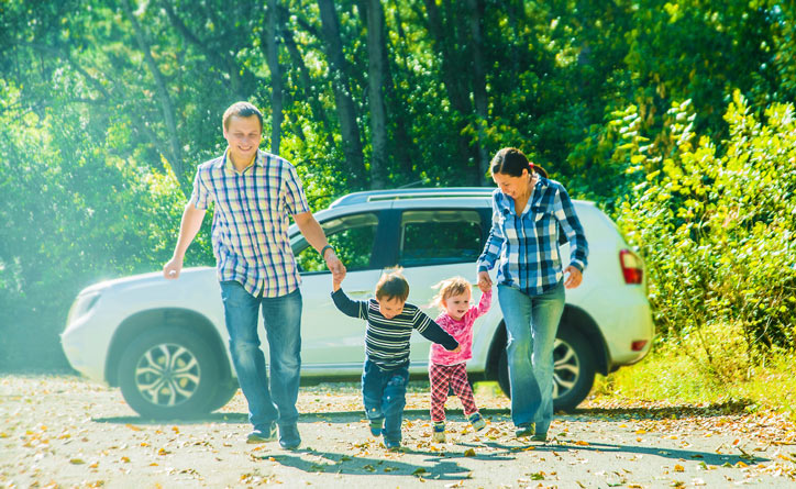 Family holding hands and walking, behind is an SUV parked